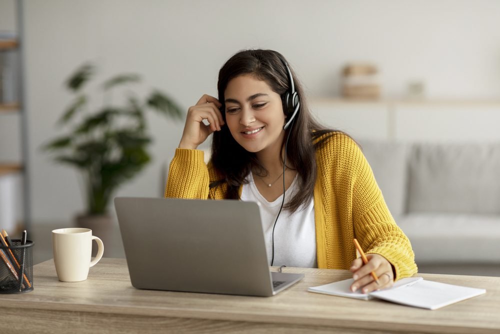 A woman wearing a sweater and headset working her Alorica work from home job