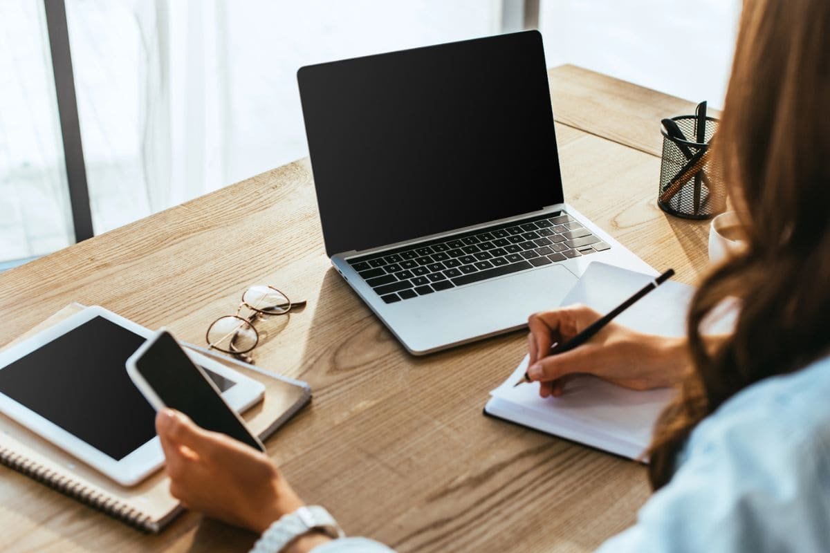 A woman working remotely from her home office, using a laptop and writing in a notebook.