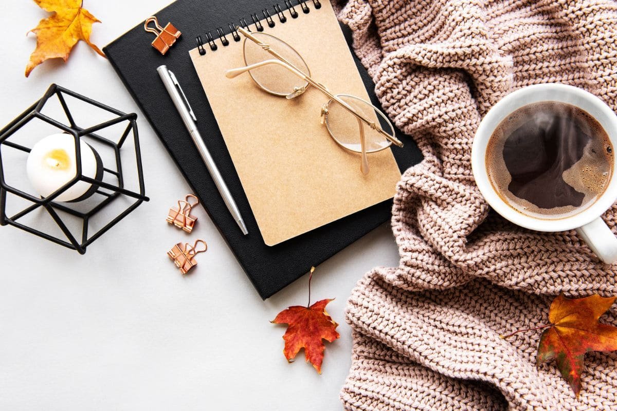 A business woman's home office desk, with a scarf, candle, notebooks, and fall leaves.