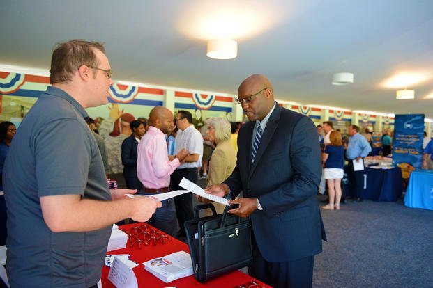 Harold Little, right, a retired Navy lieutenant, exchanges paperwork with a company representative during a large-scale military job fair in Ponte Vedra Beach, Florida.